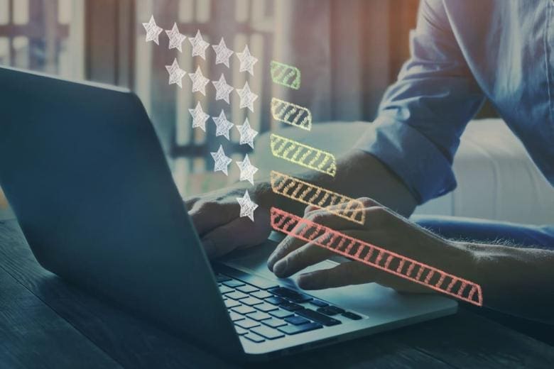 Person typing on a laptop with a holographic star rating graphic above the keyboard, showing colored stars across five rating lines. The scene is indoors with soft daylight filtering through a window in the background, implying tools to manage and remove negative Google reviews efficiently.