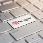 A close-up of a computer keyboard with the "Enter" key replaced by a white key featuring the Instagram logo and text. The surrounding keys are grey, and soft light highlights the keyboard.